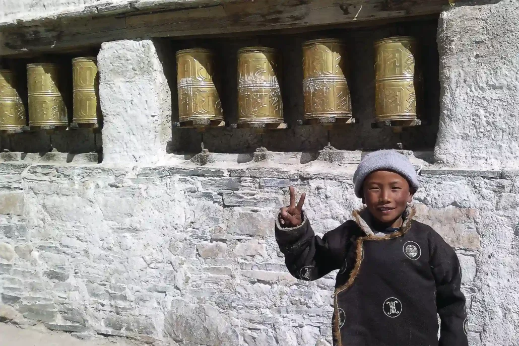 Niño haciendo el gesto de la victoria junto a un mani wall en Tibet