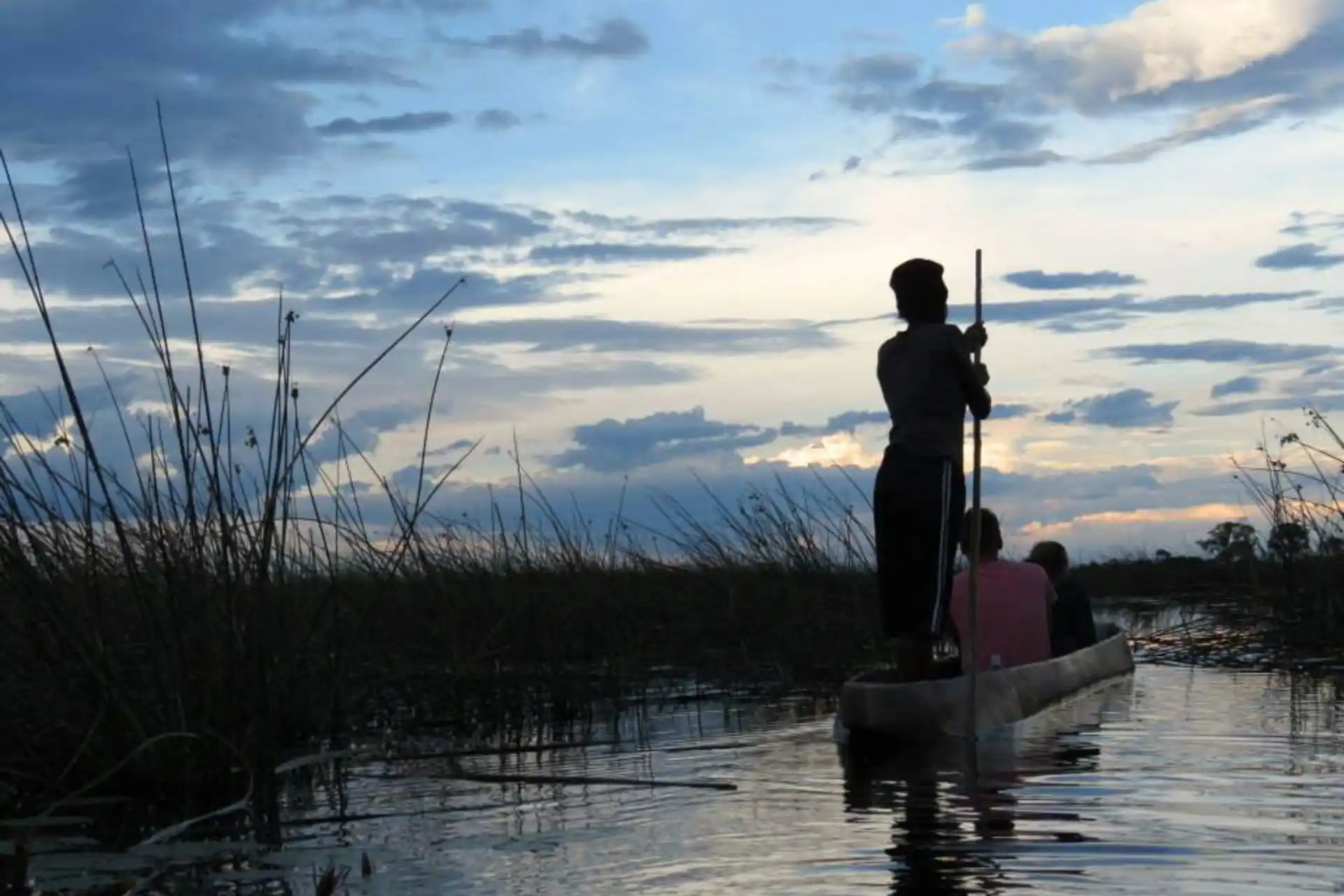 Viajeros en un mokoro navegando por el delta del Okavango al atardecer durante un viaje organizado a Botswana