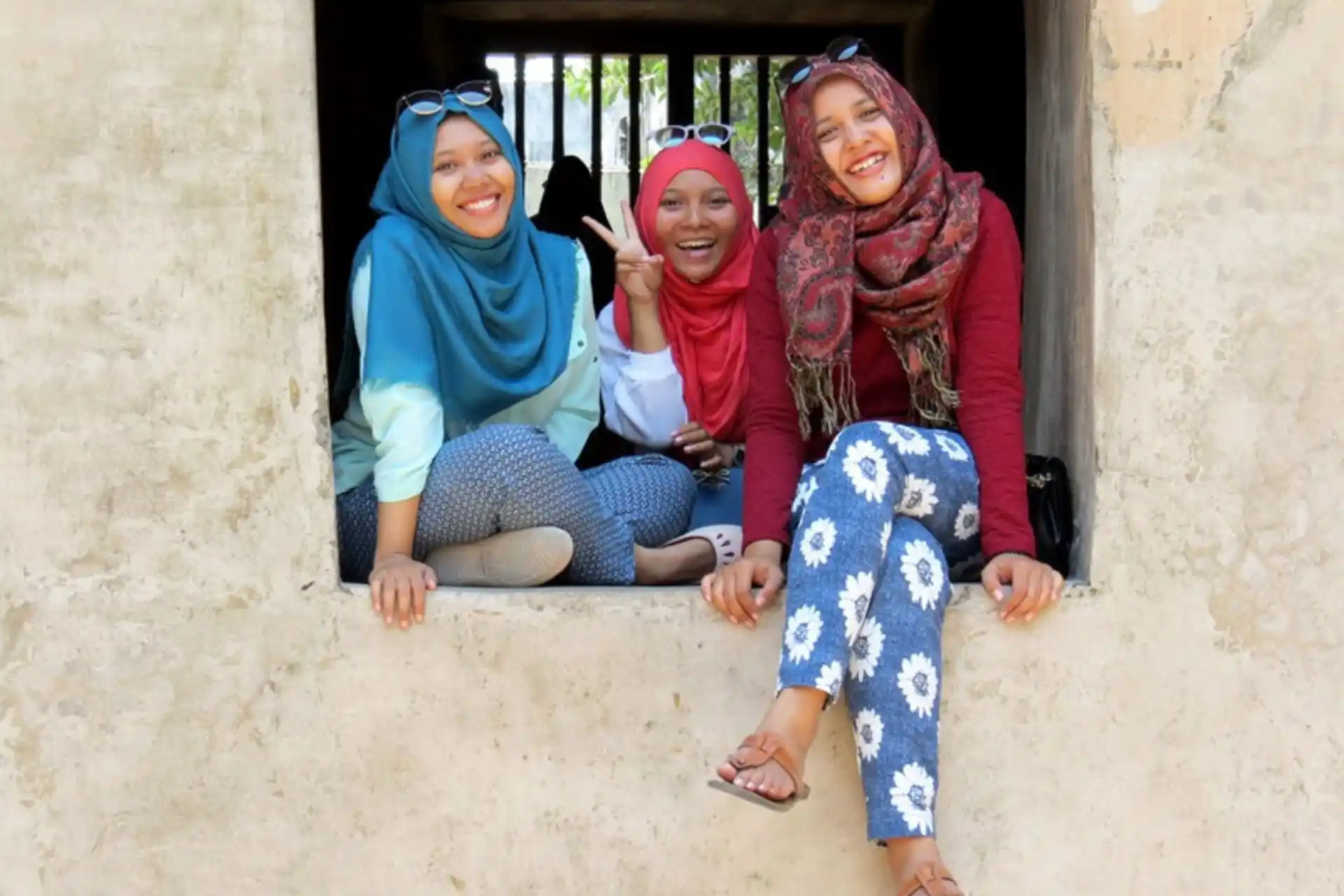 Tres mujeres indonesias sentadas en el quicio de una ventana sonriendo a la cámara