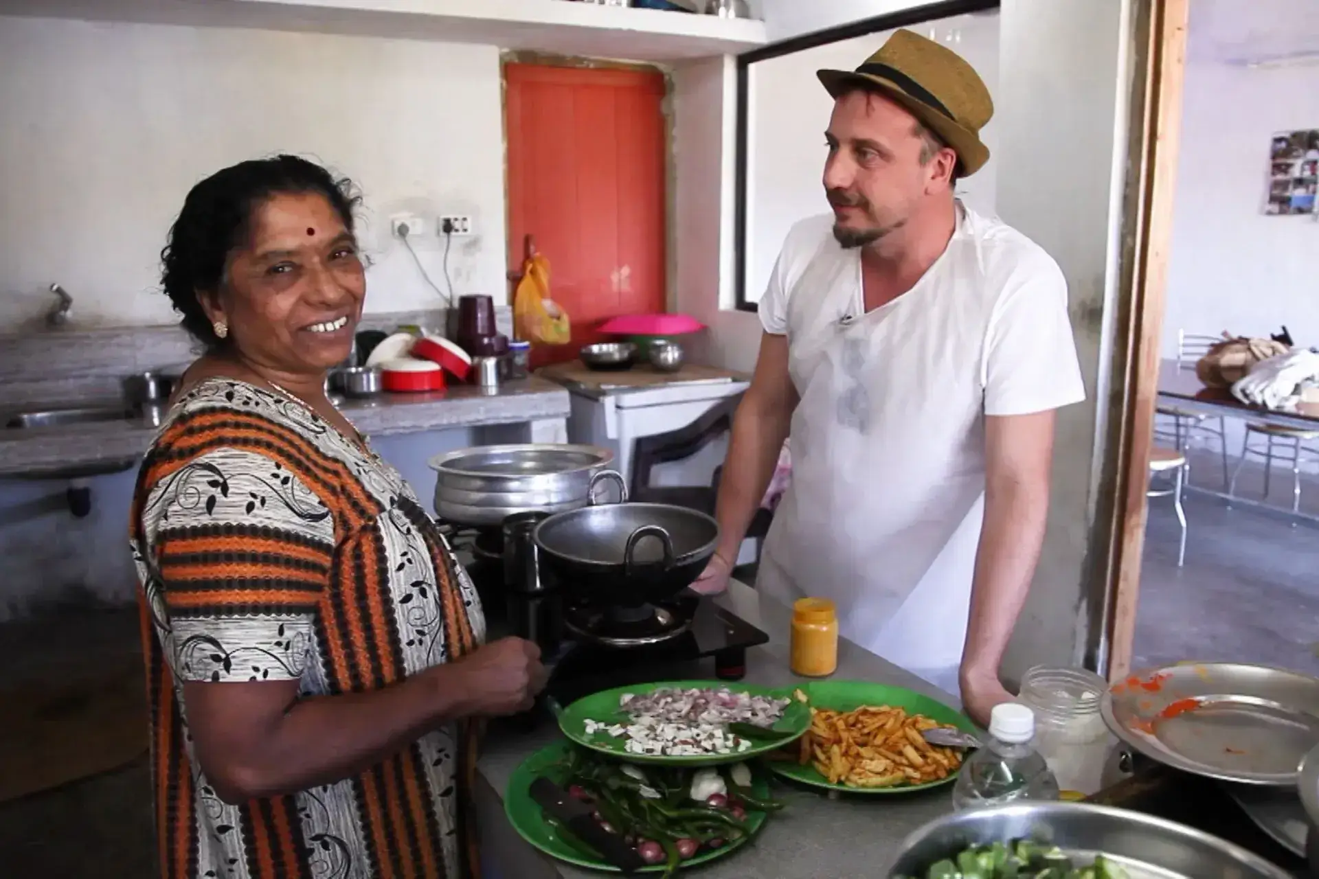 Mujer india y hombre blanco con sombrero conversan en torno a una mesa con comida