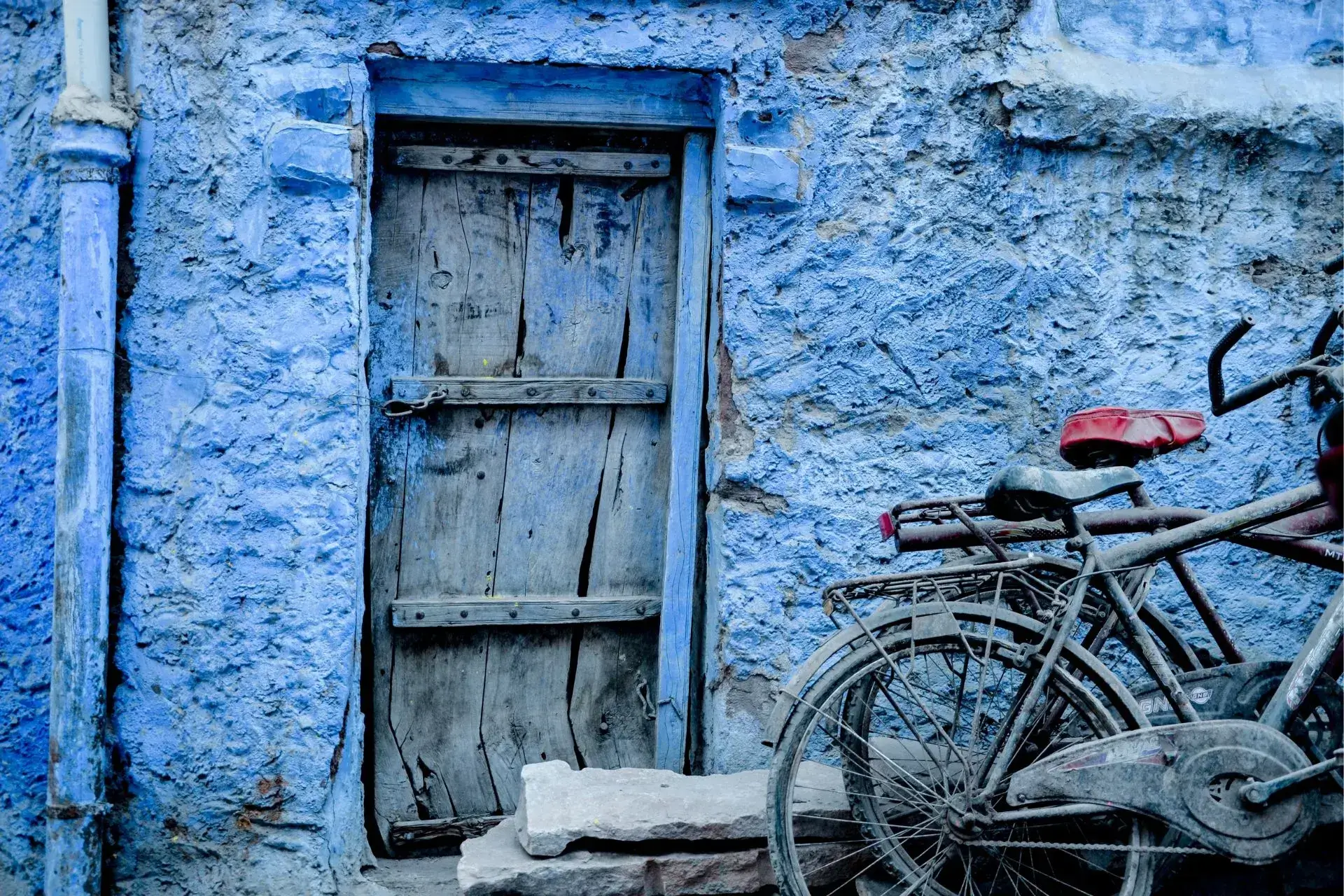 La pared de una casa y su puerta de madera pintadas de azul y una bicicleta apoyada