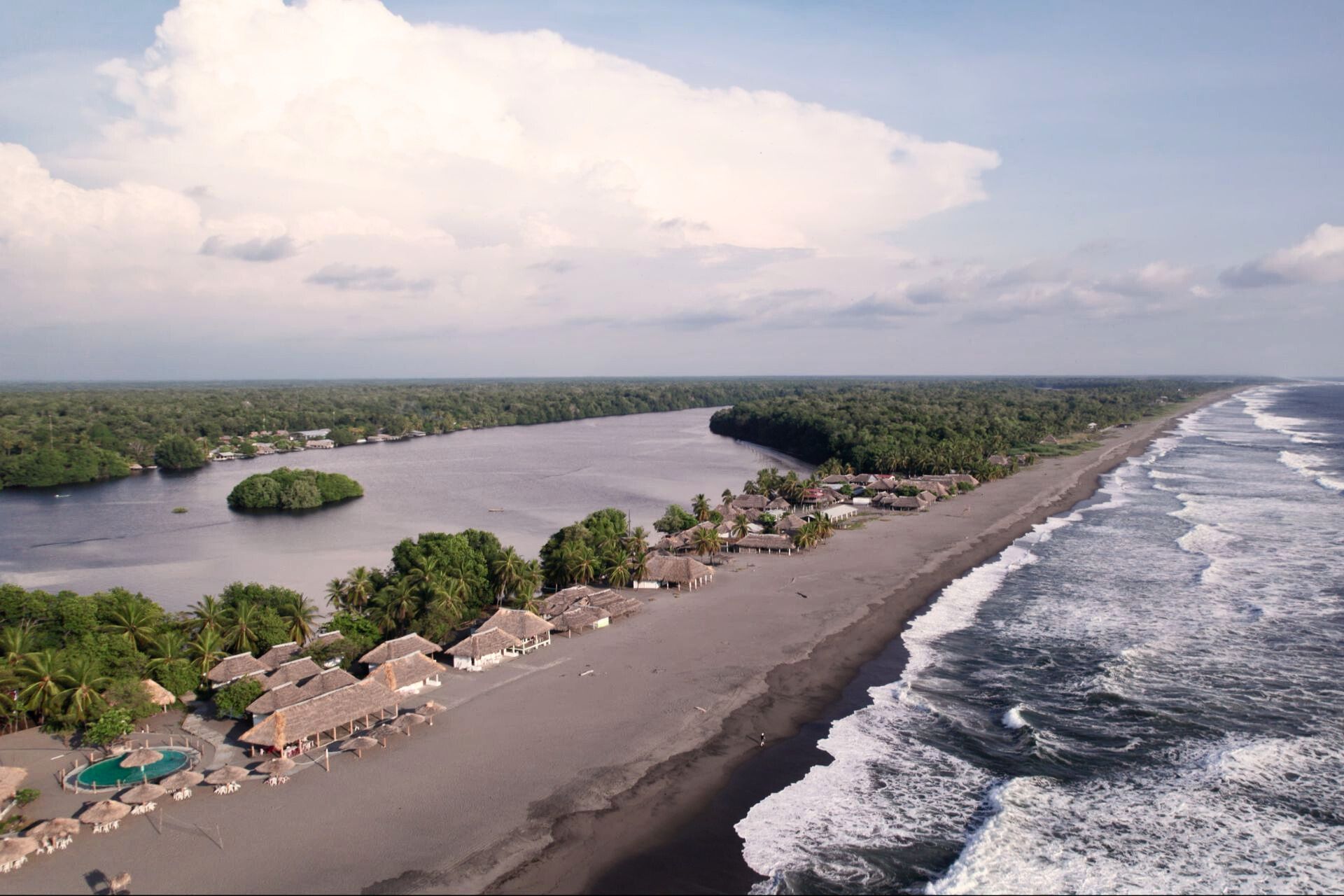 Playa con sombrillas y palmeras, por un lado tiene el mar y al otra una ría en Chiapas