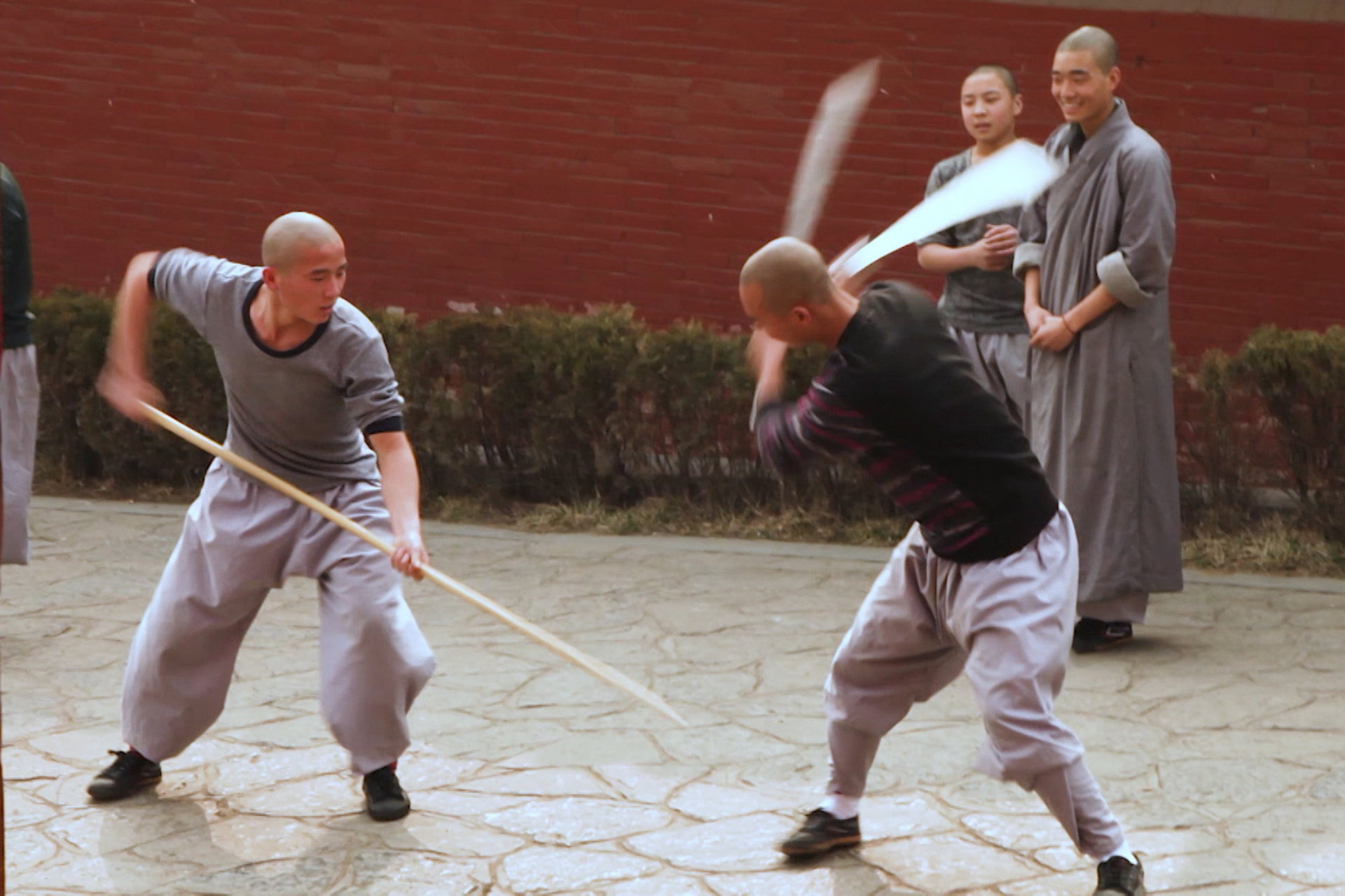 Dos hombres practicando artes marciales, uno sujeta un palo y el otro una espada