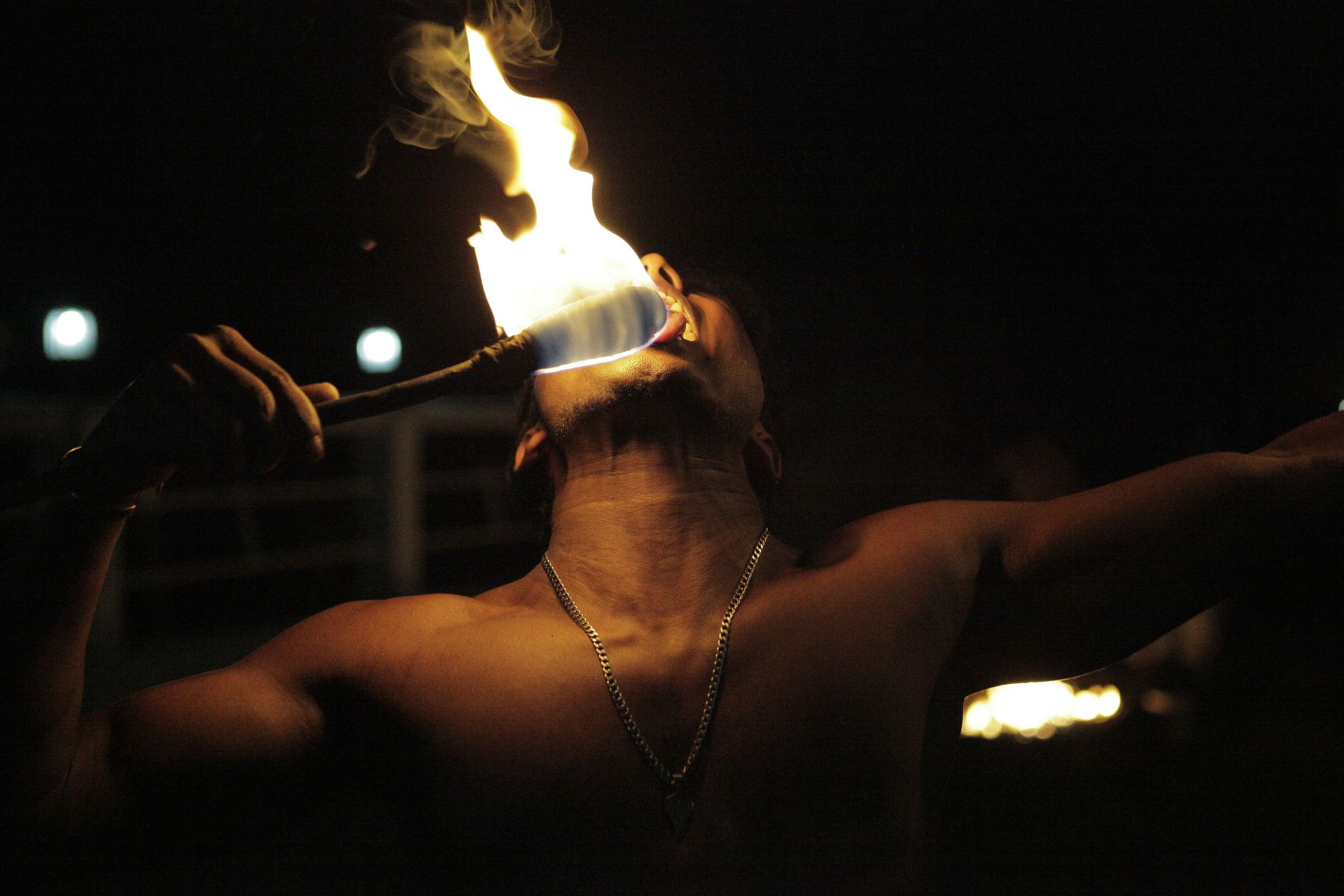 Hombre en la oscuridad sosteniendo un palo con fuego en el extremo y cerca de su boca