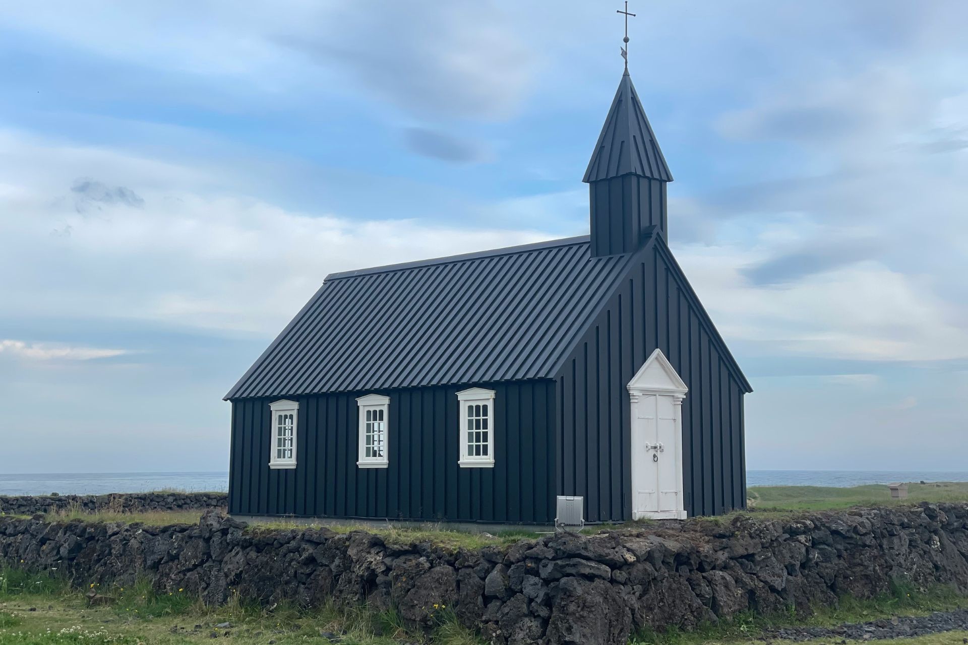 Iglesia negra con ventanas blancas y al fondo el mar