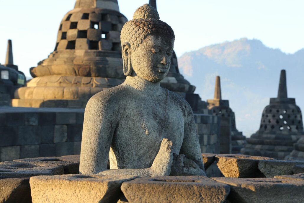 Escultura en piedra gris y manos juntas en el frente, y detrás varias esculturas en forma de campana